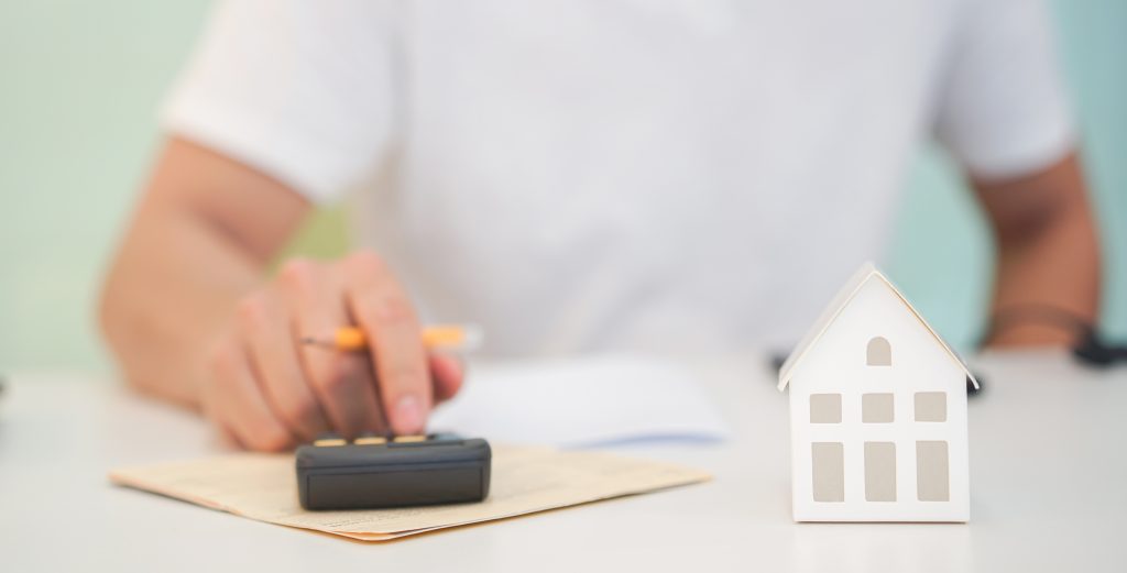 close up house's model with young man hand counting on calculator to summary of refinance expense for planning and manage money about home loan mortgage and interest rates for people lifestyle concept