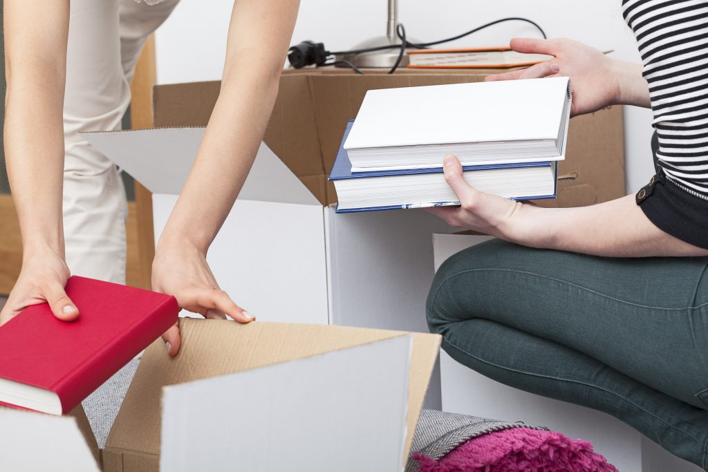 two people packing books into small white moving cartons.