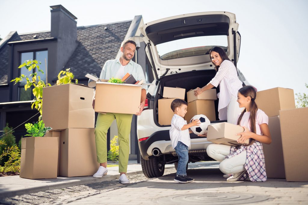 Portrait of lovely cheerful family brother sister moving to new place carrying moving boxes from house to car.