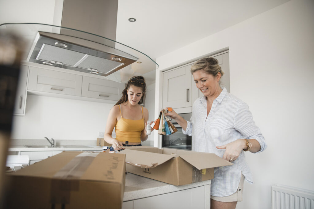 Woman and daughter standing in a kitchen packing food into moving boxes as they prepare to move.