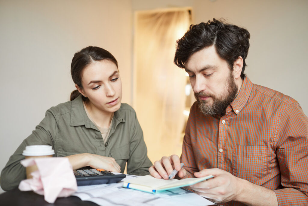 Man and woman sitting at a table with papers and calculator determining a moving budget.