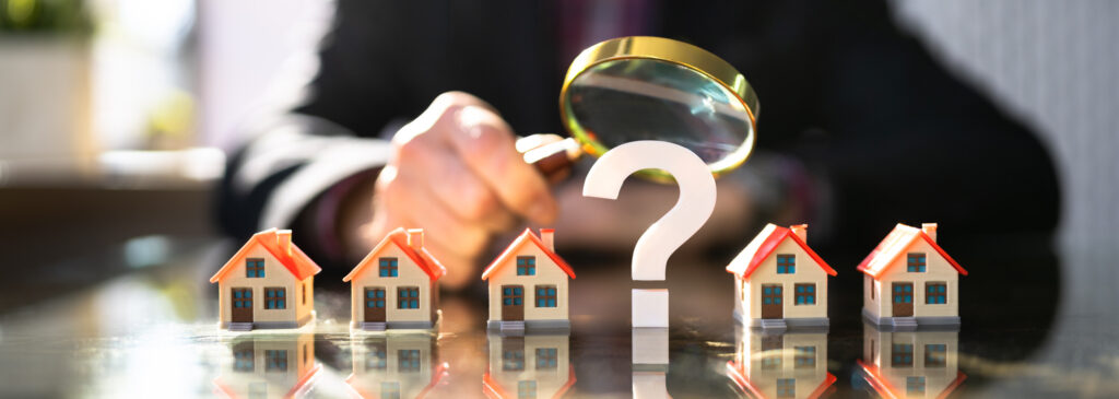 Question mark and magnifying glass among toy houses representing questions about buying a house